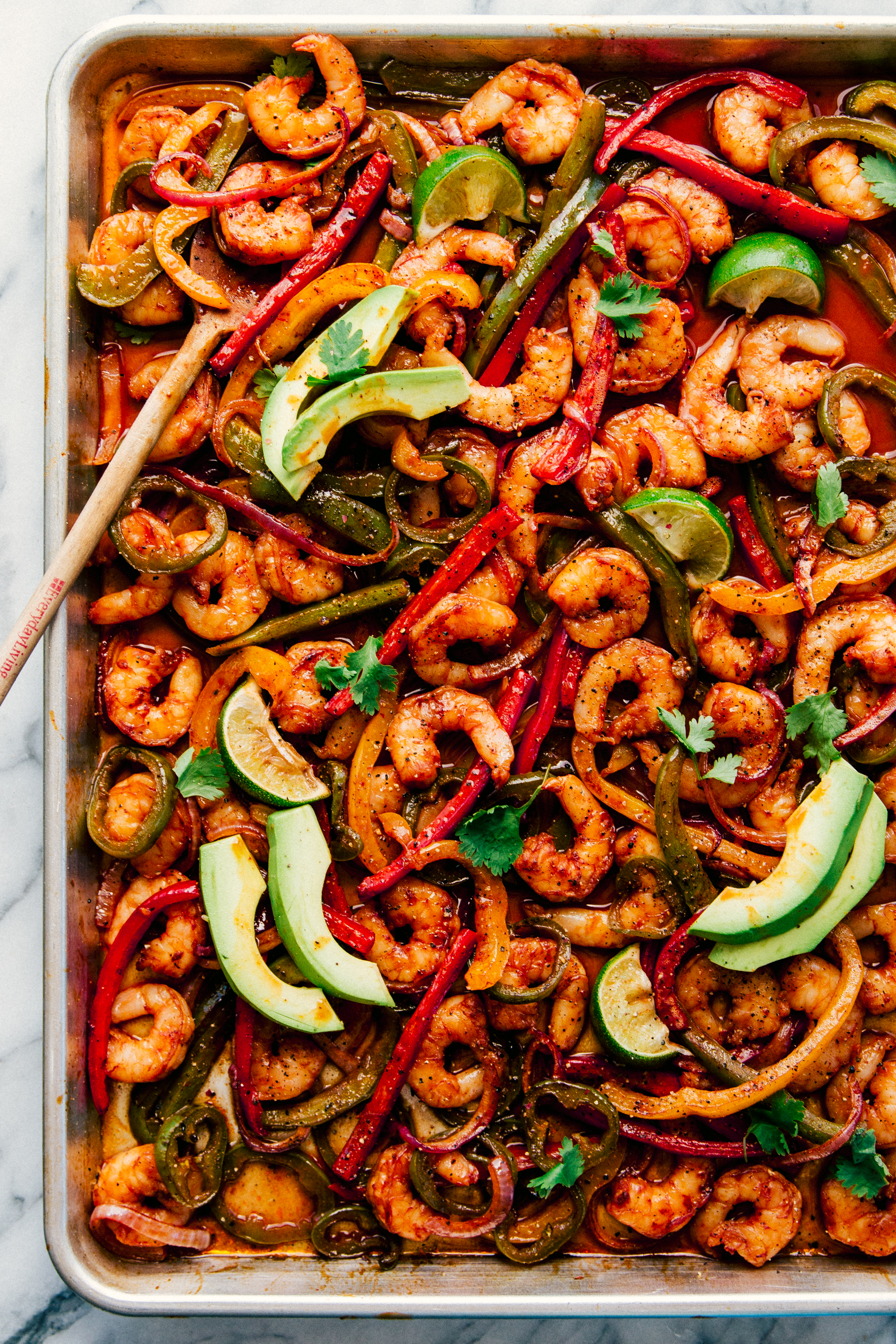 Sheet Pan Shrimp Fajitas with avocado and lime slices on a white background, by The Food Cafe