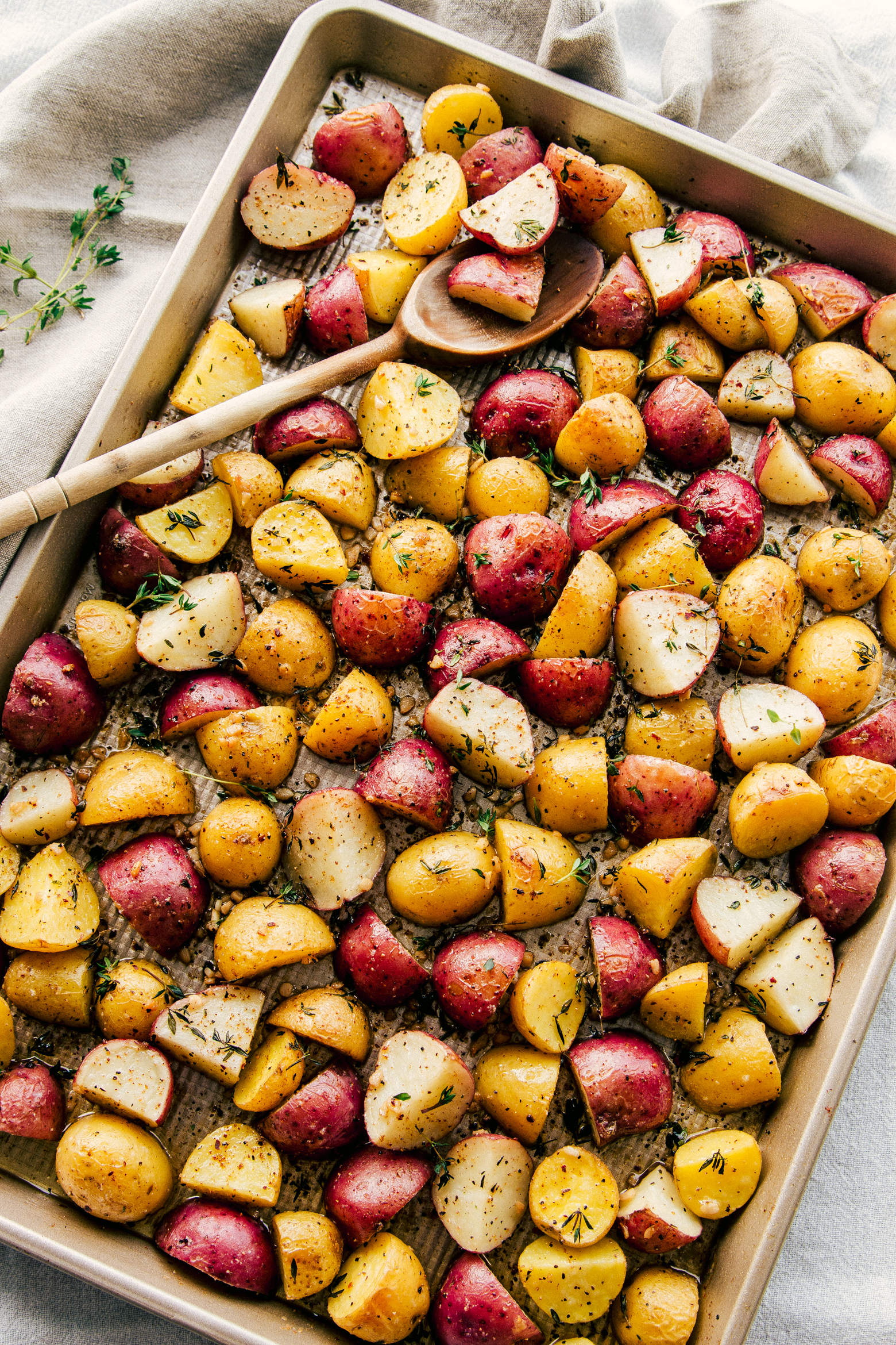  Garlic Butter Roasted Potatoes on a sheet pan with a wooden spoon for serving. 