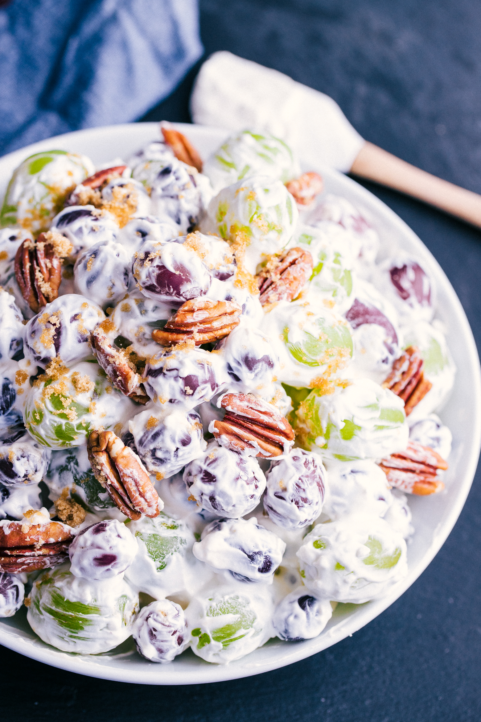creamy grape salad in a white serving bowl sprinkled with brown sugar and pecans-perfect side dish