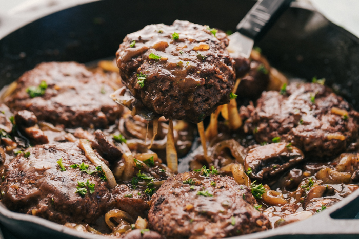 hamburger steak being lifted out of the skillet with a spatula. 