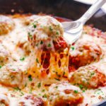 parmesan chicken meatballs in a skillet being scooped out with a large spoon.