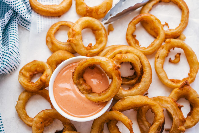 Beer Battered Onion Rings on white parchment paper with dipping sauce by The Food Cafe. 