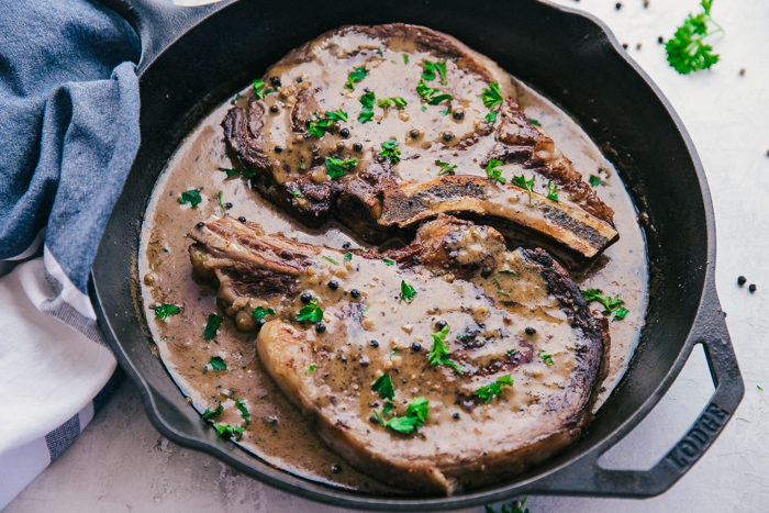 Rib Eye Steak in a cast iron skillet on a white background with a creamy peppercorn sauce the perfect simple recipe by The Food Cafe.
