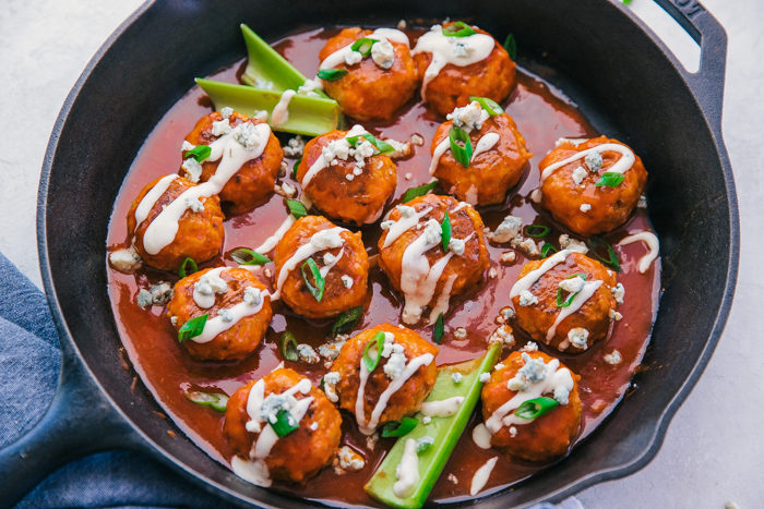 Buffalo Chicken Meatballs in a cast iron skillet with buffalo sauce and slices of celery by the food cafe. 