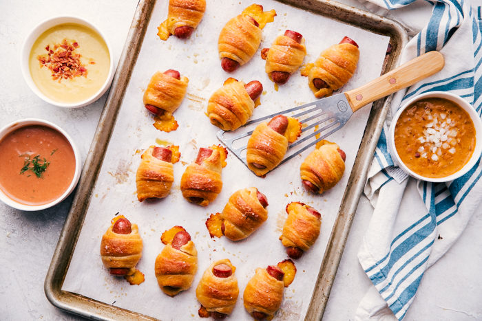 Cheesy Pigs in a Blanket on a sheet pan with dipping sauce.