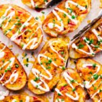 cheddar and bacon potato skins on a sheet pan being served with thongs.