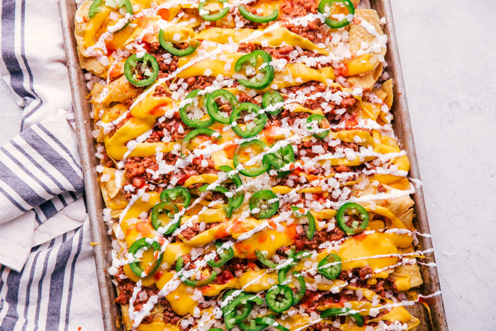 chili cheese nachos served on a sheet pan topped with onions, jalapeños, cheese, and sour cream by The Food Cafe. 