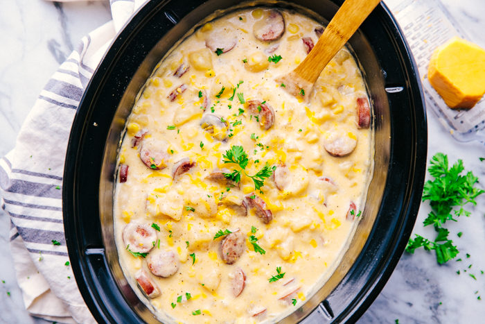slow cooker sausage and potato soup being served from slow cooker with wooden spoon. 