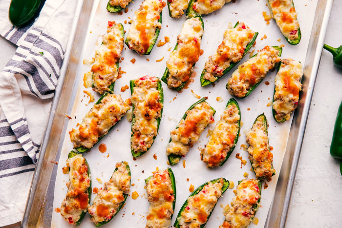 Stuffed Jalapeno Poppers on a sheet pan drizzled with hot sauce.