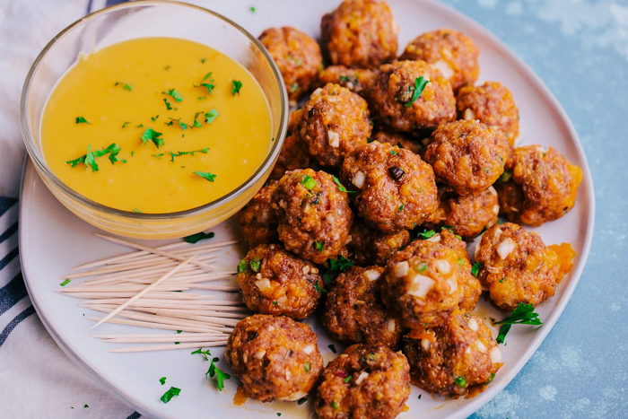 spicy sausage cheese balls on a white plate with cheese dip and toothpicks.