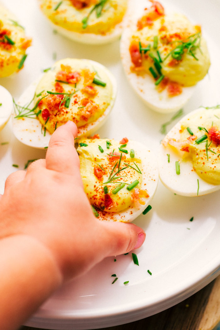 bacon ranch deviled eggs on a white plate being removed by a little girl to eat-kid friendly finger food. 