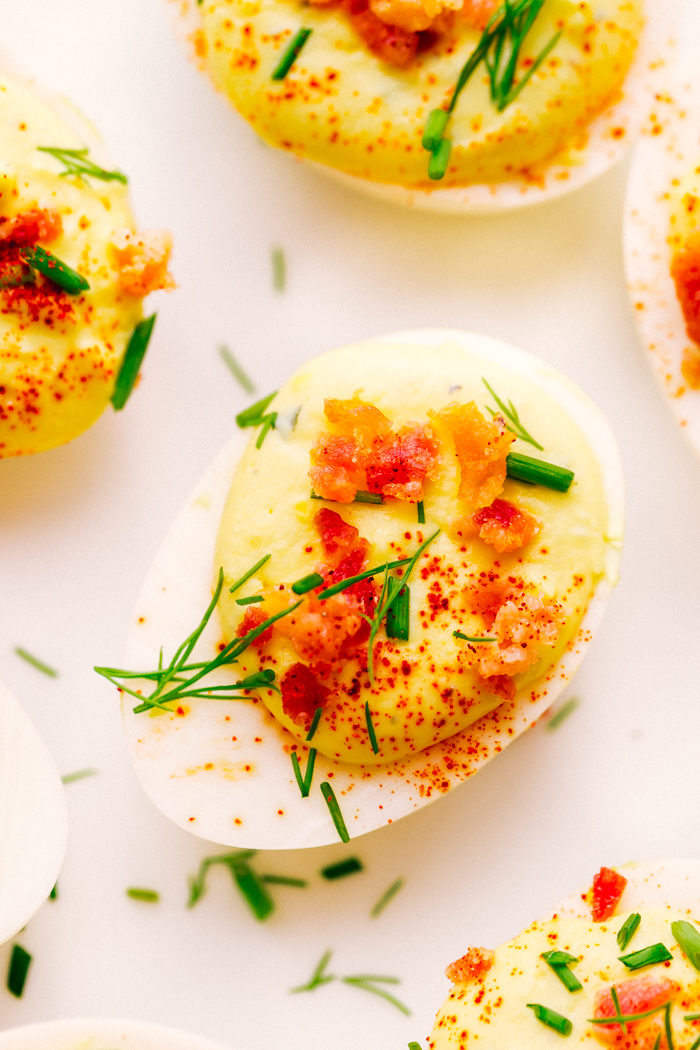 bacon ranch deviled egg on a white plate garnished with bacon, dill, and chives. 