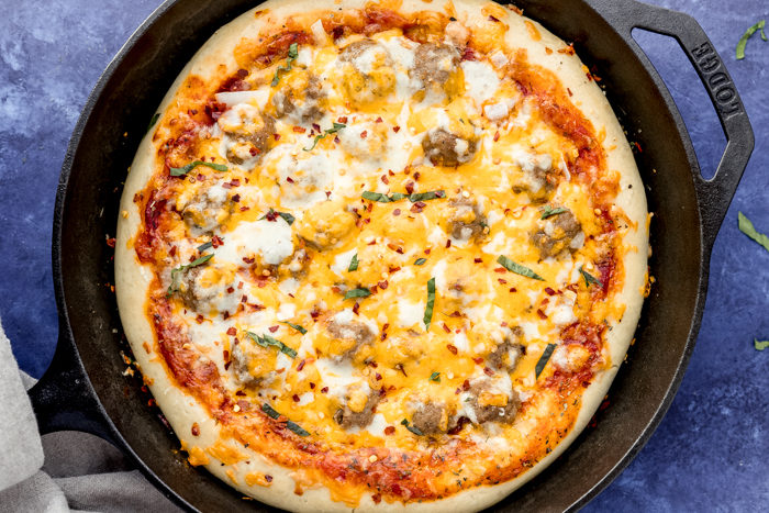 Meatball pizza by the food cafe in a cast iron skillet with a blue background topped with cheese and chopped basil-easy dinner idea. 