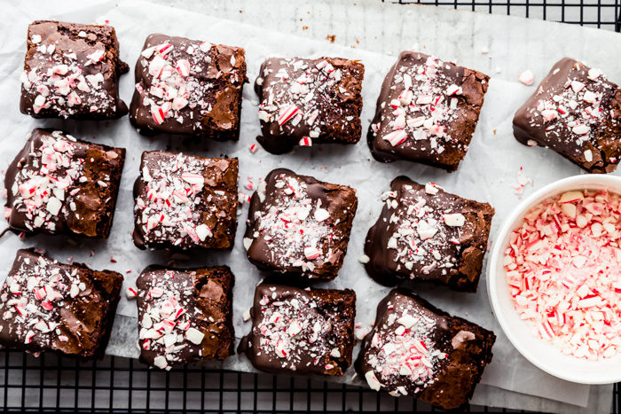 Peppermint brownies dipped in chocolate and topped with crushed candy cane cut into squares on a cooling rack lined with parchment paper, quick and easy by The Food Cafe