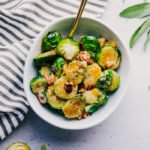 Brussels sprouts casserole in a white bowl served with a gold spoon on a white background.