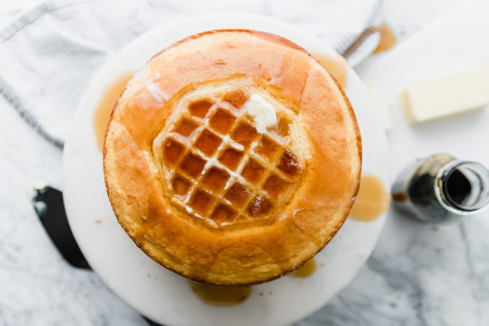 waffle cake from an overhead view on a white background with melted butter and maple syrup poured on top, with maple syrup and butter in the background and a black serving spatula, by The Food Cafe