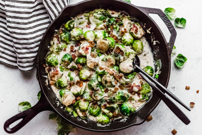 A black cast iron skillet on a white background with roasted brussels sprouts being served with a black spoon by The Food Cafe. 