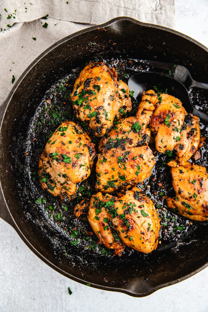 Honey garlic chicken in a black cast iron skillet topped with fresh cut parsley