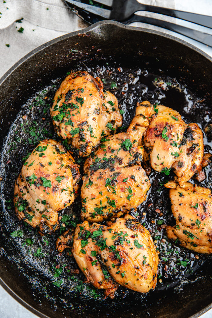Honey garlic chicken thighs in a black skillet topped with fresh parsley and honey garlic sause